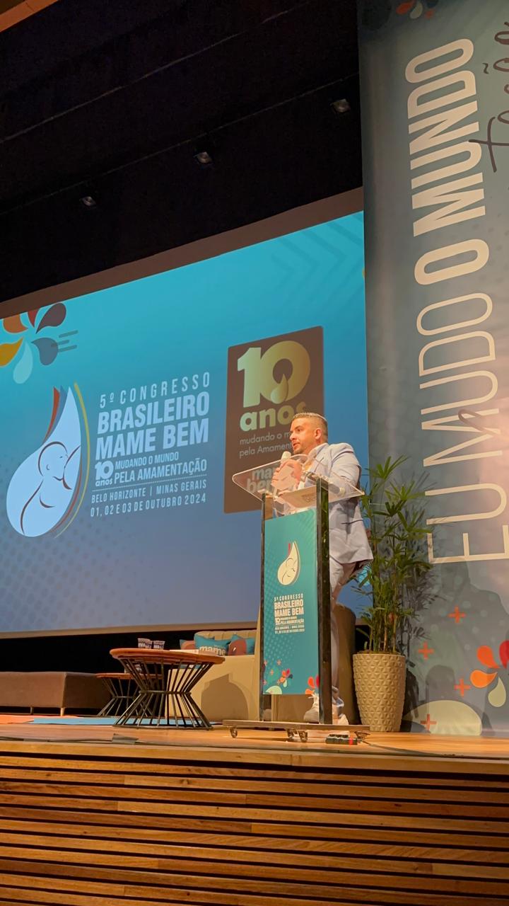 Dr. Henrique Veneroso no palco do Congresso Brasileiro Mame Bem, falando ao púlpito diante do telão do evento